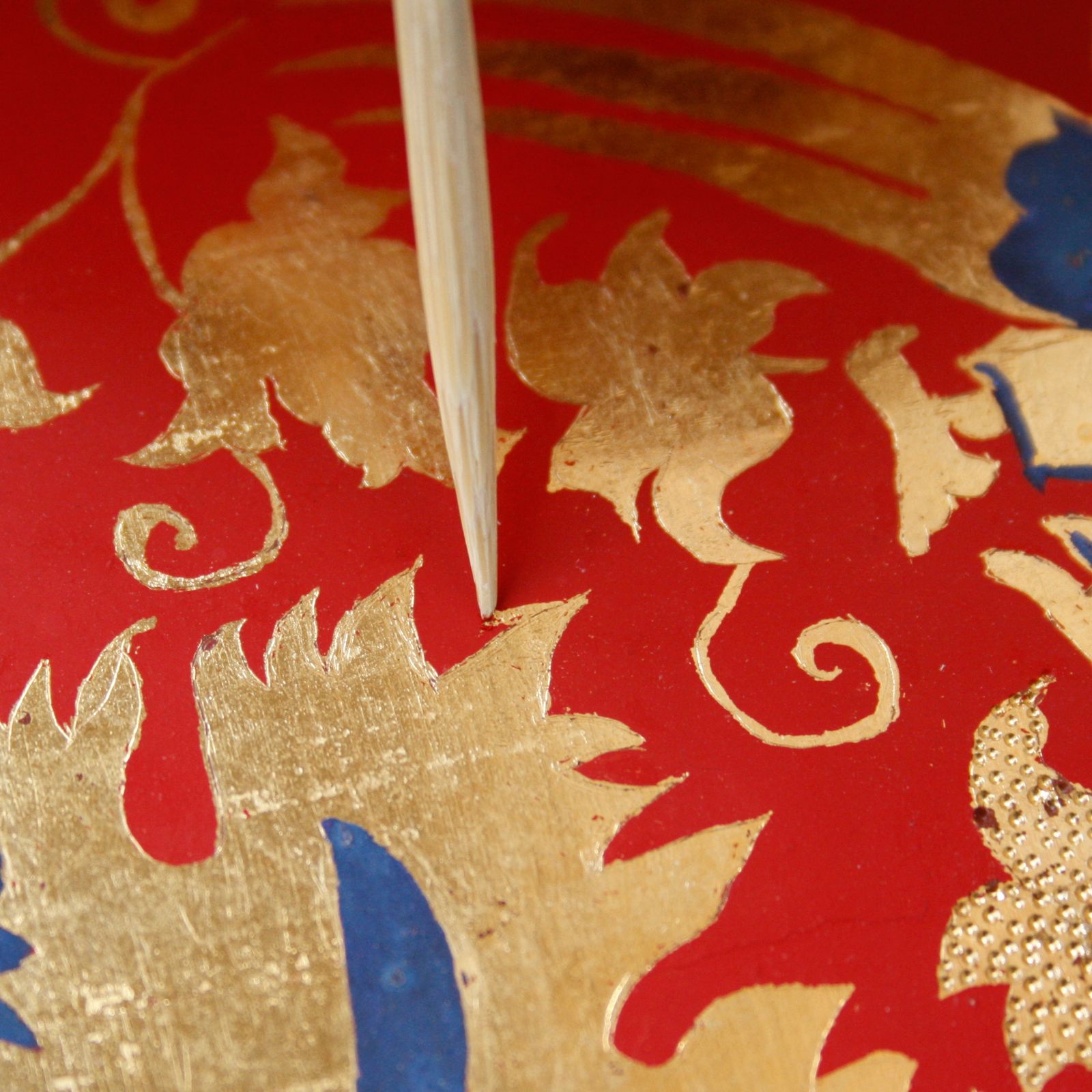 The patterns are made using sgraffito. Red paint is scraped away using a bamboo stick, revealing the gold underneath